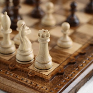 May include: A wooden chessboard with a carved design and a set of white chess pieces, including a rook, a knight, and a pawn. The chessboard is closed and has a brass latch.