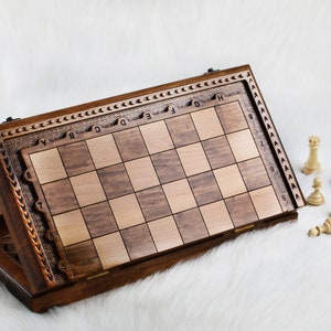 May include: A wooden chessboard with a carved design on the side. The board is open and the pieces are scattered around it. The pieces are made of wood and are painted in black and white.