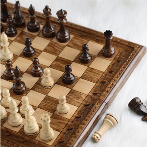 May include: A wooden chessboard with brown and light wood squares. The board is open and shows a game in progress with black and white chess pieces. The pieces are made of wood and have a polished finish.