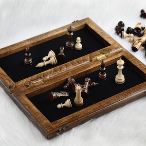 May include: A wooden chessboard with a black felt interior and a hinged lid. The board is open and some chess pieces are scattered on the felt surface. The chess pieces are made of wood and are painted in black and white.