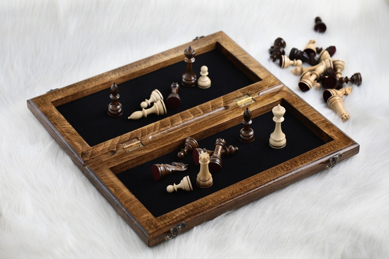 May include: A wooden chessboard with a black felt interior and a hinged lid. The board is open and some chess pieces are scattered on the felt surface. The chess pieces are made of wood and are painted in black and white.