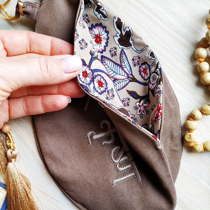 May include: A brown fabric pouch with a floral print lining. The pouch has the word "Trust" embroidered on the front.