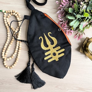 May include: Black fabric pouch with a gold embroidered symbol, a trishula, and a tassel. The pouch has an orange lining and a small metal ring.