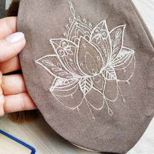 May include: A brown fabric pouch with a white embroidered mandala design. The mandala features a lotus flower with intricate details.
