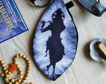 May include: A black fabric pouch with a white silhouette of a figure playing a flute. The figure is surrounded by a white radial pattern. The pouch is hanging from a black strap.