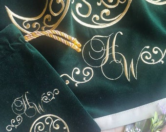 Könnte beinhalten: Ein grüner Samtbeutel mit einer goldenen gestickten Mondsichel und dem Text "H&W". Der Beutel wird mit einer goldenen Kordel geschlossen und liegt auf einer weißen Oberfläche.