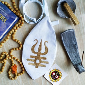 May include: A white fabric pouch with a gold embroidered symbol of a trident and three horizontal lines. The pouch is tied with a white cord and has a small, round, gray stone with a wooden stick inside.