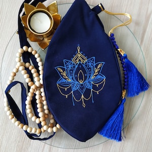 Könnte beinhalten: Eine dunkelblaue Stofftasche mit einem goldenen, gestickten Lotusblüten-Design. Die Tasche hat einen langen Riemen mit einem blauen und goldenen Quasten.