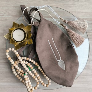 May include: A brown fabric pouch with a white beaded design, a string of wooden beads, a small candle in a gold lotus holder, and a beaded tassel.