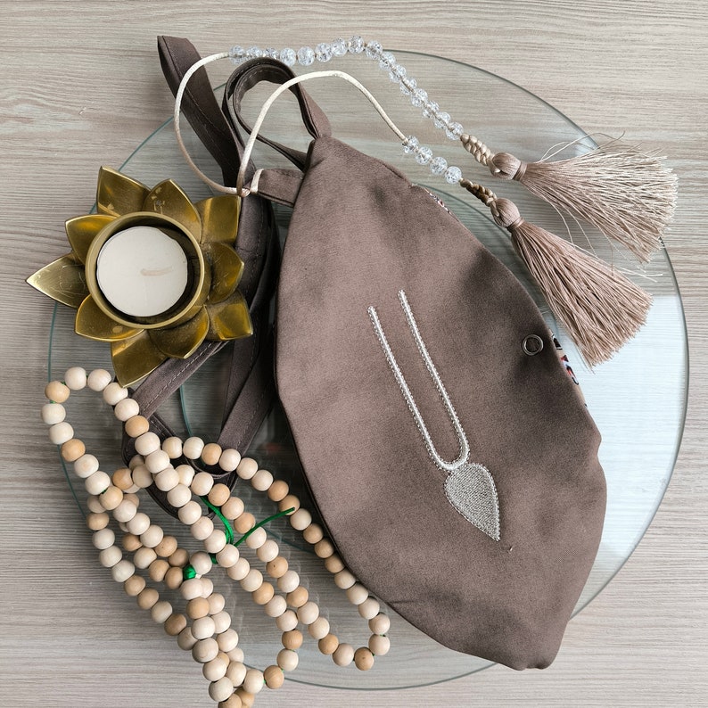 May include: A brown fabric pouch with a white beaded design, a string of wooden beads, a small candle in a gold lotus holder, and a beaded tassel.