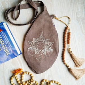 May include: A brown canvas bag with a long strap and a white embroidered lotus flower design. The bag has a tassel on the strap.