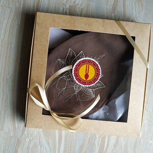 May include: A brown fabric gift box with a gold ribbon and a white tag with a red and yellow design. The tag has a fork and spoon symbol and the text "U" in the center.