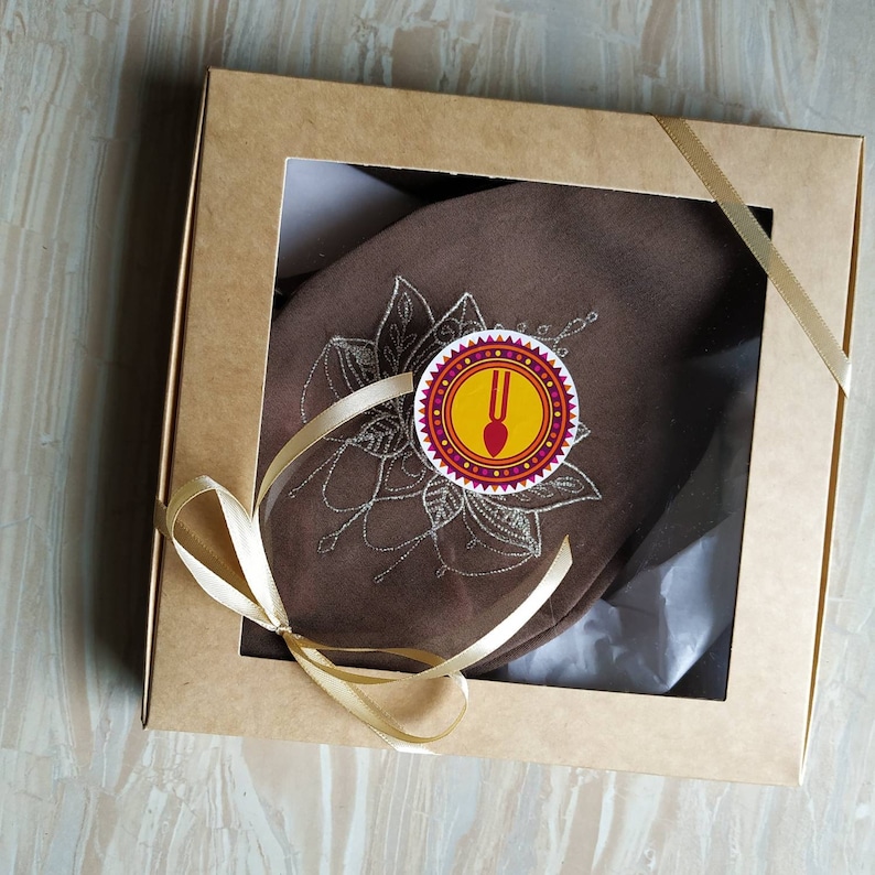 May include: A brown fabric gift box with a gold ribbon and a white tag with a red and yellow design. The tag has a fork and spoon symbol and the text "U" in the center.