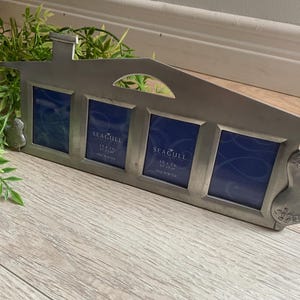 Puede incluir: Un marco de fotos de metal plateado con forma de casa con cuatro aberturas para fotos. El marco tiene un diseño decorativo en el lateral y las palabras "Seagull 4x6" impresas en la parte inferior de cada abertura.