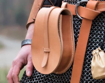 May include: A person wearing chainmail armor with a brown leather belt and a brown leather pouch attached to the belt. The pouch has a flap with a buckle. There is a small gold pouch hanging from the belt.
