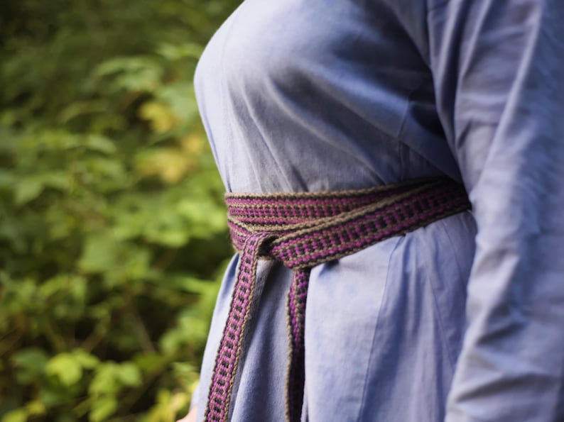 Op de afbeelding: Een blauw shirt met een geweven paarse en bruine riem om de taille.