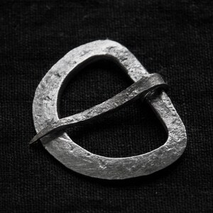 May include: A silver metal buckle with a simple, curved design. The buckle is made from a single piece of metal, with a smooth, polished finish.