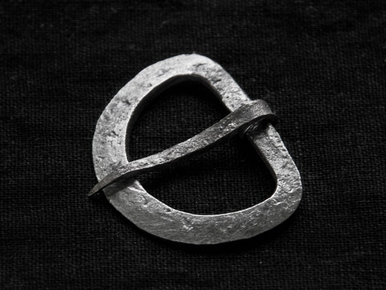 May include: A silver metal buckle with a simple, curved design. The buckle is made from a single piece of metal, with a smooth, polished finish.