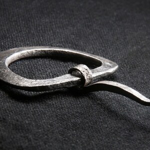 May include: A silver metal ring with a curved tail. The ring is made of thick, hammered metal and has a rough, textured surface.