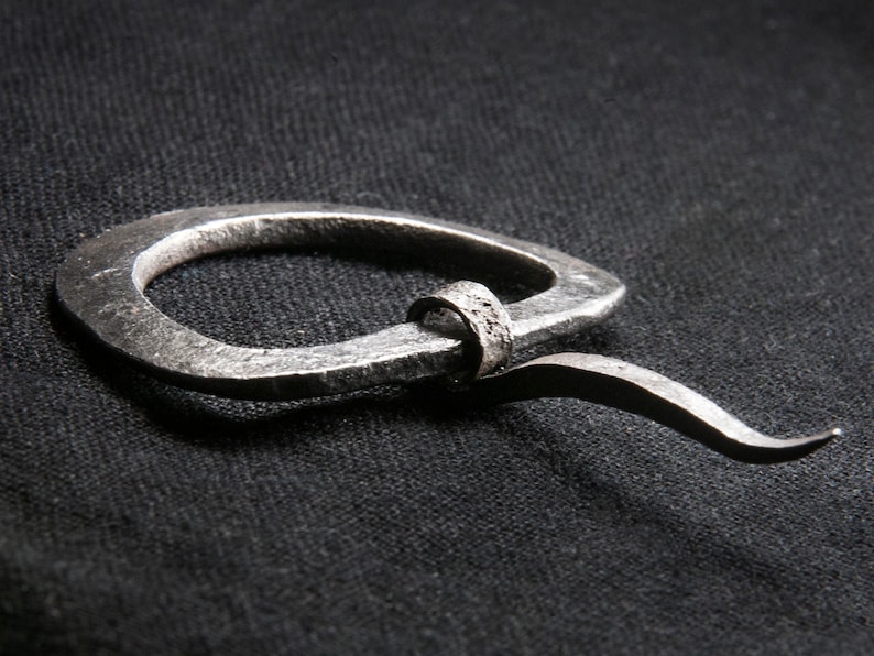May include: A silver metal ring with a curved tail. The ring is made of thick, hammered metal and has a rough, textured surface.