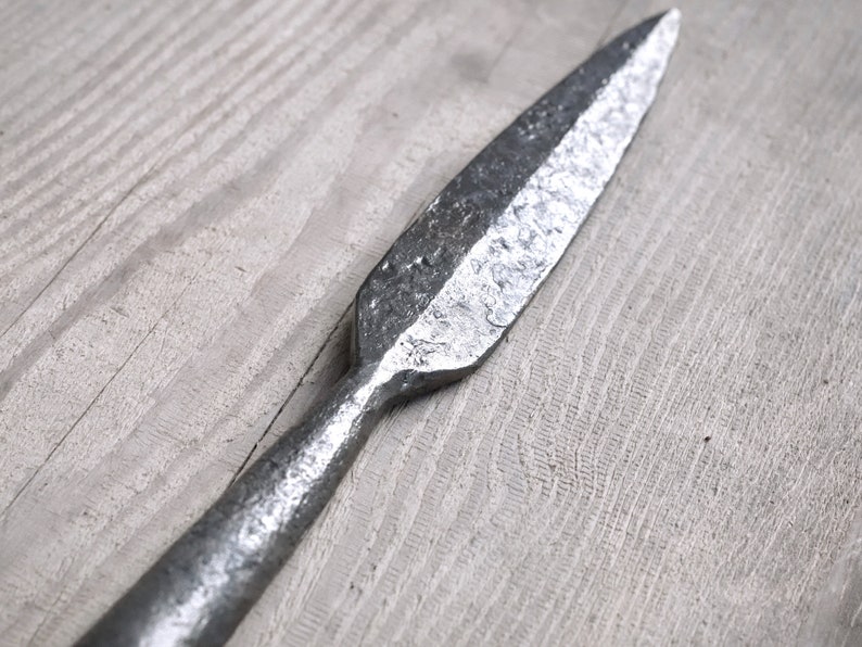 Może przedstawiać: Srebrna metalowa grot wł&oacute;czni z ostrym końcem i szorstką, fakturowaną powierzchnią.