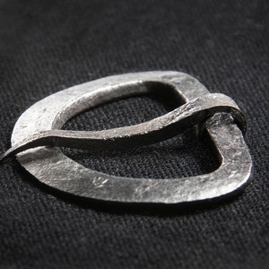 May include: A silver metal buckle with a unique, curved design. The buckle is made from a single piece of metal and has a smooth, polished finish.