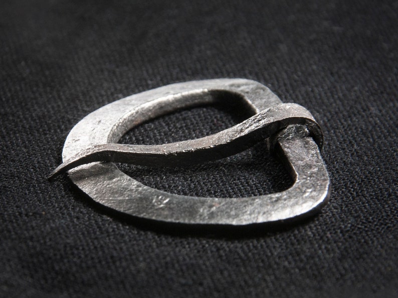 May include: A silver metal buckle with a unique, curved design. The buckle is made from a single piece of metal and has a smooth, polished finish.
