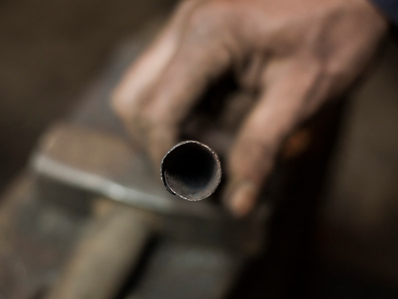May include: Close-up of a metal pipe being held by a hand. The pipe is round and has a dark gray finish.