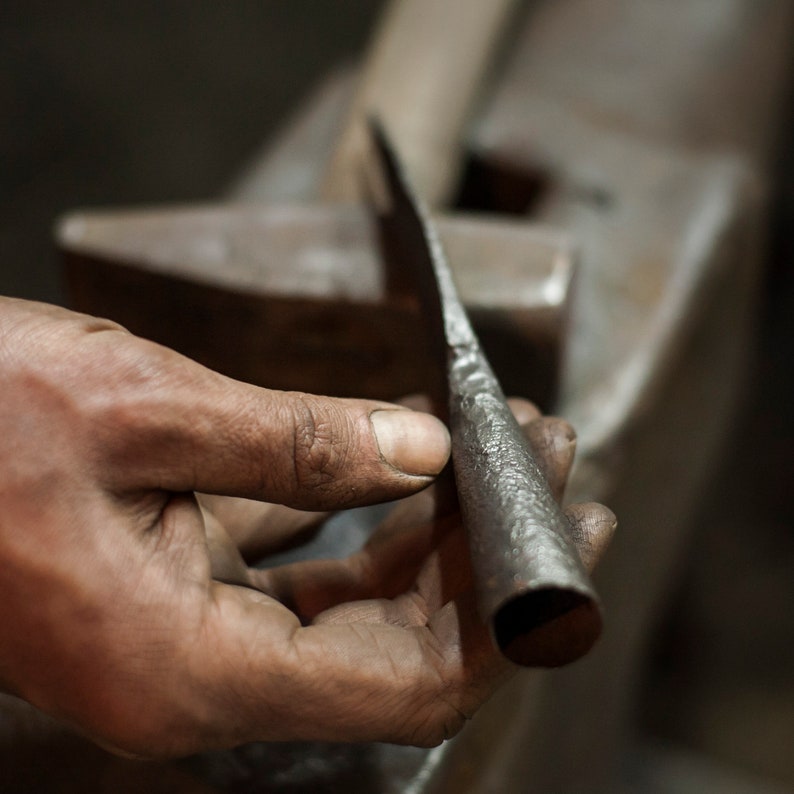 May include: A close-up of a hand holding a long, thin, metal rod with a rounded end. The rod is dark gray and has a textured surface. The hand is holding the rod near the rounded end, and the rod is pointing towards the right side of the image.