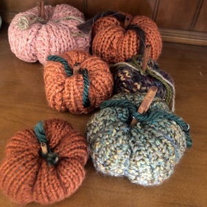 May include: Five knitted pumpkins in various colors, including pink, orange, and green. The pumpkins are decorated with cinnamon sticks for stems.