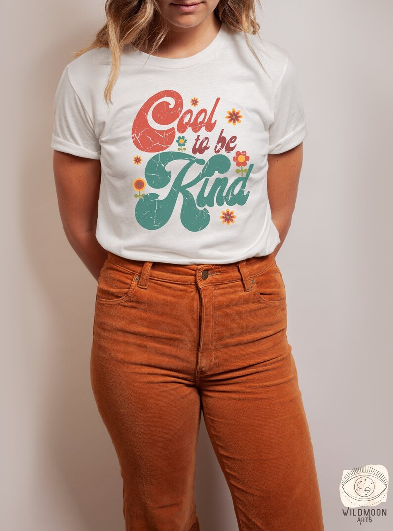 Pode incluir: Uma t-shirt branca de manga curta com o texto Cool to be Kind numa fonte vermelha e verde desgastada, decorada com pequenas ilustra&ccedil;&otilde;es de flores coloridas. A t-shirt &eacute; combinada com cal&ccedil;as de veludo cotel&ecirc; cor de laranja com fecho.