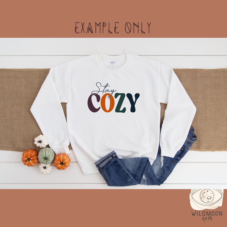 Peut inclure: Sweat-shirt blanc avec le texte "Stay Cozy" en lettres majuscules color&eacute;es. Les lettres sont dans des tons de violet, orange, vert et noir.