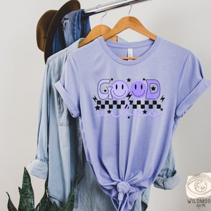 May include: A lavender t-shirt with the text "GOOD vibes" in black and white with purple smiley faces and stars.