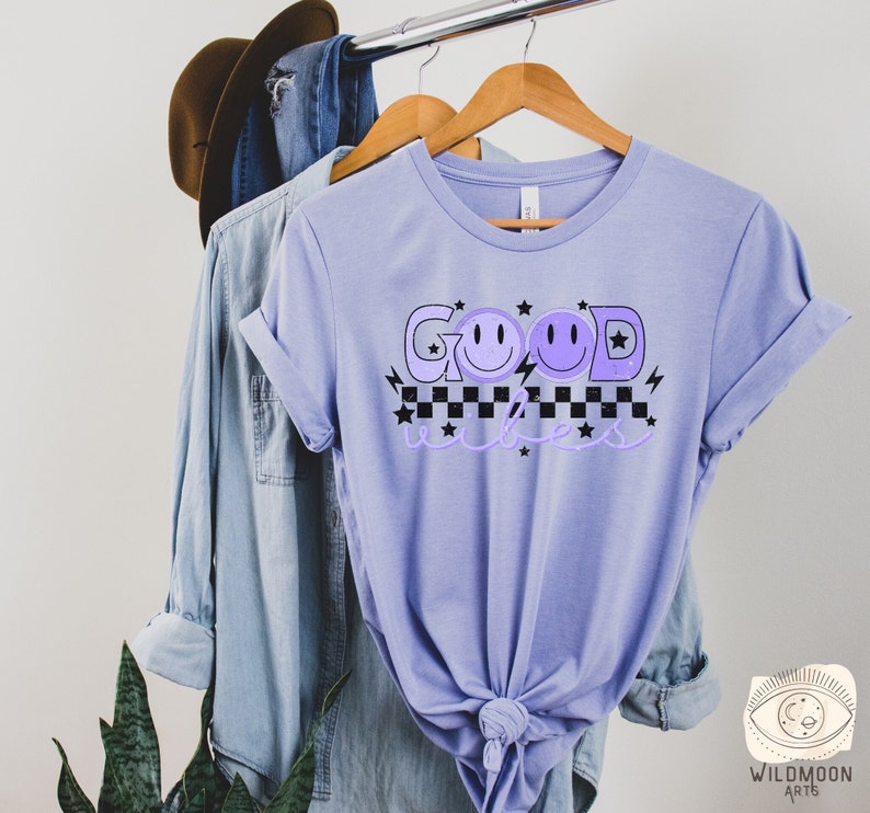 May include: A lavender t-shirt with the text "GOOD vibes" in black and white with purple smiley faces and stars.