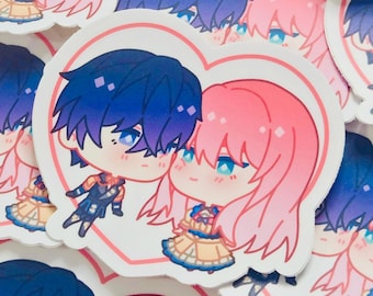 May include: A collection of heart-shaped stickers featuring anime-style illustrations. Each sticker showcases a couple with blue and pink hair, blue eyes, and detailed outfits. The stickers have a pink heart outline.