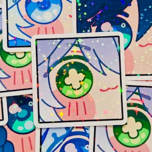 Pode incluir: Autocolantes quadrados com um desenho de olho de desenho animado. Os autocolantes apresentam uma borda branca e um acabamento hologr&aacute;fico. O design do olho inclui cores azul, verde, rosa e branco. Os autocolantes est&atilde;o espalhados.