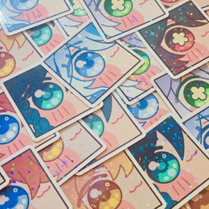 Pode incluir: Uma cole&ccedil;&atilde;o de autocolantes quadrados com desenhos de olhos estilo anime. Os olhos t&ecirc;m v&aacute;rias cores, incluindo azul, verde e castanho, com detalhes brilhantes. Os autocolantes t&ecirc;m um fundo rosa claro e uma borda branca.