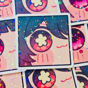 Pode incluir: Autocolantes quadrados com um design de olho estilizado e uma pupila em forma de flor. O olho tem detalhes em rosa, azul e roxo, com uma borda branca e detalhes hologr&aacute;ficos brilhantes. Os autocolantes est&atilde;o dispostos numa grelha.