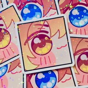 Pode incluir: Autocolantes quadrados com um design de olho de desenho animado em tons de azul, rosa e amarelo. Os autocolantes t&ecirc;m um acabamento hologr&aacute;fico e brilhante, espalhados por uma superf&iacute;cie.