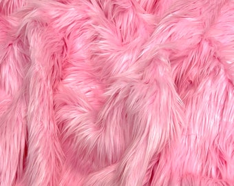 May include: Close-up of pink faux fur fabric. The fabric has long, soft, and fluffy fibres, creating a textured and luxurious appearance. The colour is a vibrant, light pink, with subtle variations in tone.