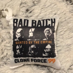 May include: White satin pillow with a black and white image of three clone troopers from Star Wars: The Bad Batch. The image has the text "Bad Batch" at the top, "Wanted by the Empire" in the middle, and "Clone Force 99" at the bottom.