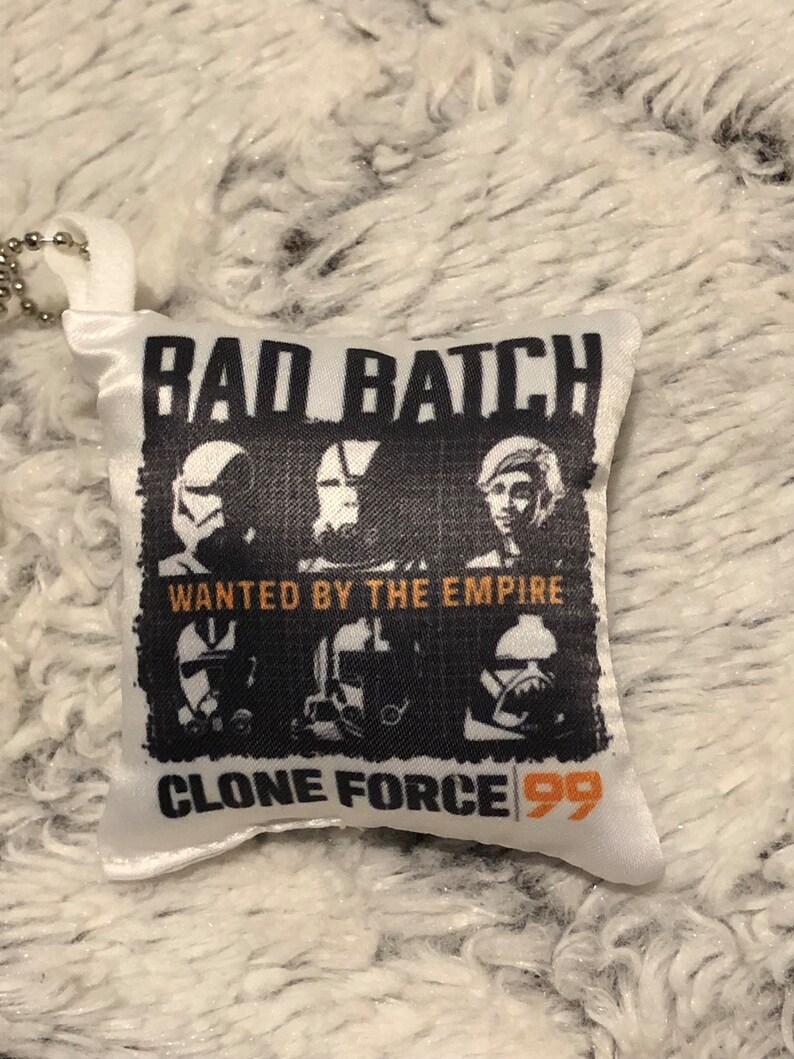 May include: White satin pillow with a black and white image of three clone troopers from Star Wars: The Bad Batch. The image has the text "Bad Batch" at the top, "Wanted by the Empire" in the middle, and "Clone Force 99" at the bottom.