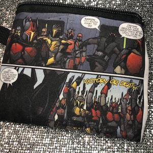 May include: A black zippered pouch with a comic book design featuring a group of characters in red and black armour. The text "VICTORY OR DEATH!" is printed in white on a black background.