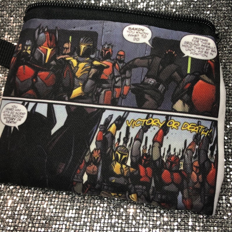 May include: A black zippered pouch with a comic book design featuring a group of characters in red and black armour. The text "VICTORY OR DEATH!" is printed in white on a black background.