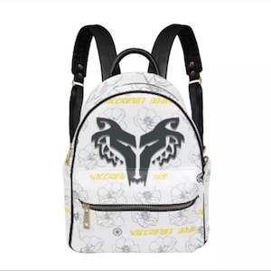 May include: White backpack with black straps and a black wolf logo on the front. The backpack has a floral pattern with yellow text that says "WAKCCHU!" on the front and back.