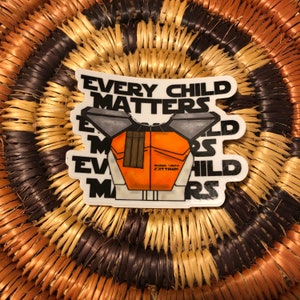 May include: White sticker with the text "Every Child Matters" in black. The sticker features a cartoon illustration of a person wearing a white and orange spacesuit with the text "WARNA - 1994 EST. TRAIN" on the suit.
