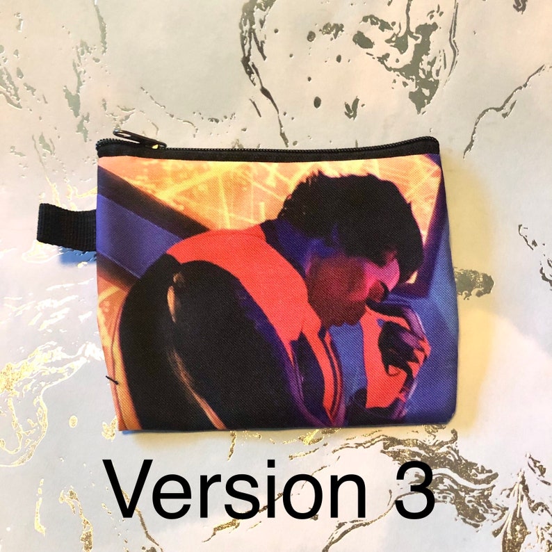 Puede incluir: Una bolsa negra con cremallera con una imagen colorida de una persona con cabello oscuro y una chaqueta roja, naranja y azul. La persona est&aacute; mirando hacia abajo y parece estar pensando.