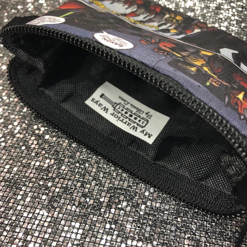 May include: A black zippered pouch with a colourful comic book design. The pouch has a label that reads "My Warrior Ways by @real_d.c."
