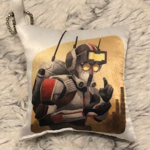 May include: A white pillow with a printed image of a cartoon character wearing a helmet and a backpack. The character is giving a thumbs up. The background is a yellow and brown desert scene.
