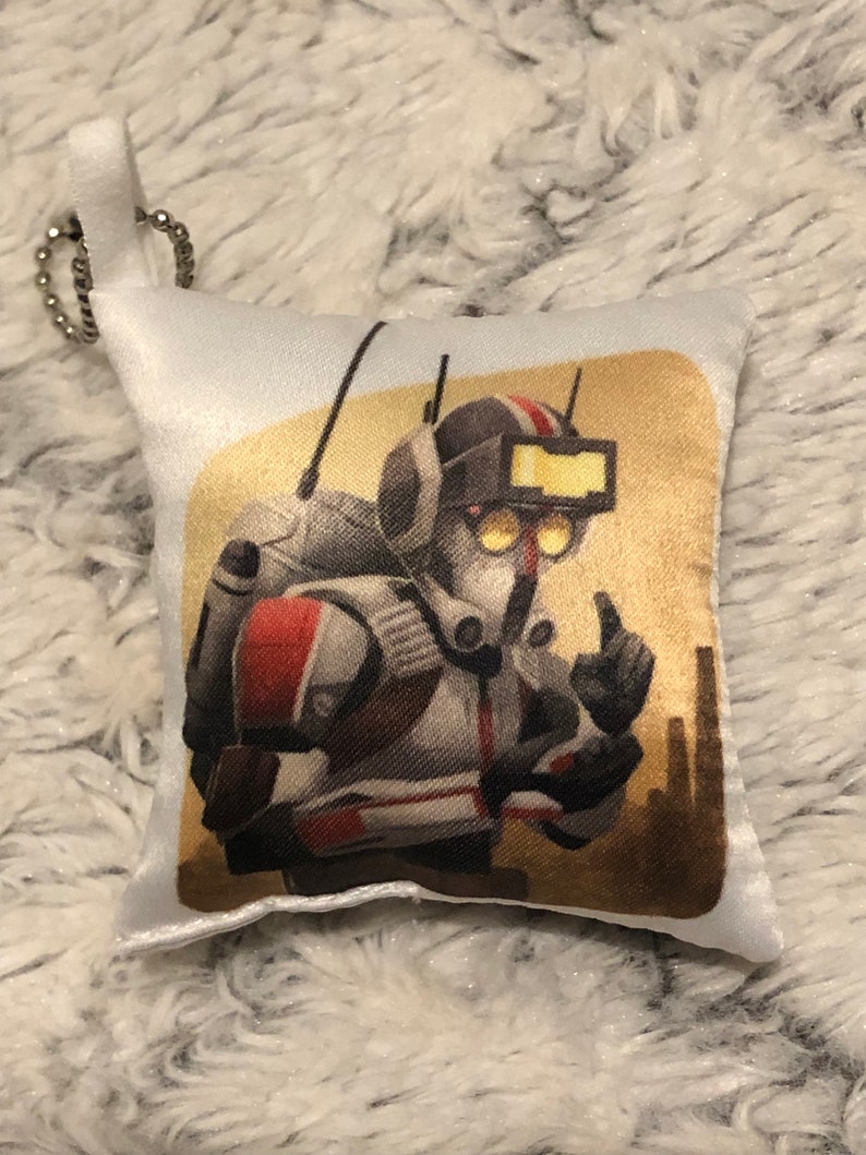 May include: A white pillow with a printed image of a cartoon character wearing a helmet and a backpack. The character is giving a thumbs up. The background is a yellow and brown desert scene.